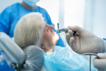  male dentist surgeon in uniform with assistant doing operation for install dental implant teeth of...