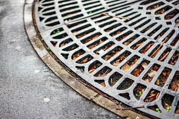 A metal grate is on the ground with leaves and dirt on it