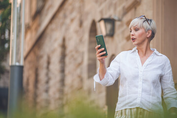 Surprised adult woman looking to his mobile phone at reading exciting message while standing...