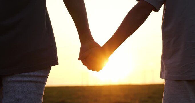 Mother and child hold hands tightly outdoors at sunset.Silhouette of hands intertwine with warmth and show love protection.Mom kid hands highlight family bond.Golden light creates peaceful atmosphere