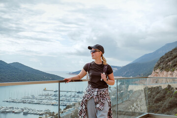 Solo eco travel moment: female traveler captures a scenic ocean view on her phone at a cliff viewpoint. Mindful, sustainable, low-impact adventure with backpack, smartwatch and freedom vibes. Thrive.