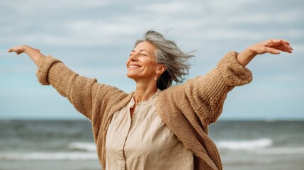 happy mature woman with arms outstretched feeling the breeze at beach beautiful middle aged woman with arms up dancing on beach mid lady feeling good and enjoying freedom at sea copy space no logos n