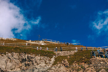 Stunning panoramic view of a cable car ascending Mount Pilatus in the Swiss Alps. The bright red gondola contrasts beautifully with the rugged mountain cliffs, lush green slopes, and distant snow-capp © Breg