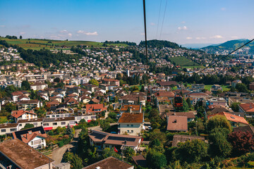 Stunning panoramic view of a cable car ascending Mount Pilatus in the Swiss Alps. The bright red gondola contrasts beautifully with the rugged mountain cliffs, lush green slopes, and distant snow-capp © Breg