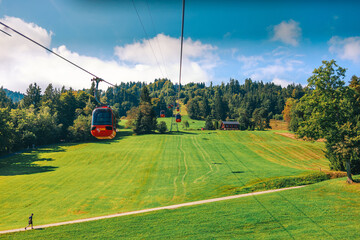 Stunning panoramic view of a cable car ascending Mount Pilatus in the Swiss Alps. The bright red gondola contrasts beautifully with the rugged mountain cliffs, lush green slopes, and distant snow-capp © Breg