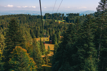 Stunning panoramic view of a cable car ascending Mount Pilatus in the Swiss Alps. The bright red gondola contrasts beautifully with the rugged mountain cliffs, lush green slopes, and distant snow-capp © Breg