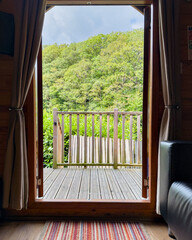 Looking out from a wooden cabin through the open door towards lush forest scenery.