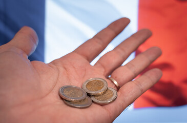 Hand showing few euro cents with France flag on background, representing poverty, financial crisis,...