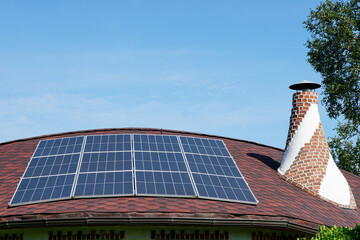Solar panels installed on a curved red roof with chimney under blue sky, renewable energy concept
