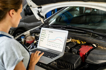 Female auto mechanic using laptop to inspect vehicle in workshop. Car performance graphs.