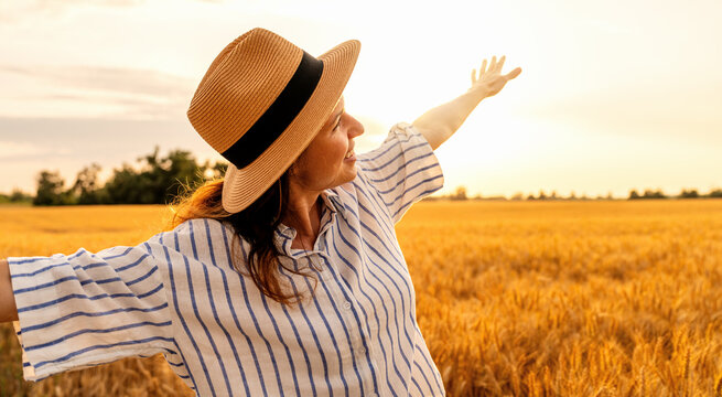 Happy woman enjoying rural nature in wheat field at golden hour light