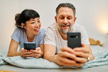 Fototapeta premium Portrait of a lovely young couple or friends having fun together using a mobile phone in bed at home