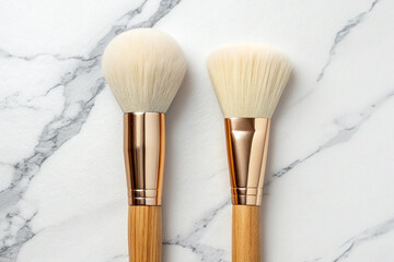 Two fluffy makeup brushes with rose gold ferrules and wooden handles on a marble background