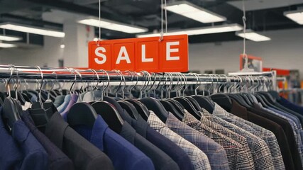A "SALE" sign hangs over a rack filled with suits, stock footage.
