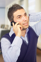 A young professional man conversing on a phone while holding a relaxed pose in a bright office...