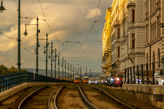 Low-angle view of Sz&eacute;chenyi rakpart tram tracks extending into perspective with distant trams, traffic jam, and historic-style lamps in warm evening light. Budapest, Hungary.

