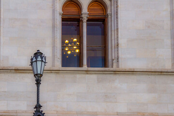 Fototapeta premium Window of Hungarian Parliament building with chandelier inside and decorative street lamp outside. Neo-Gothic architecture detail in Budapest, Hungary.
