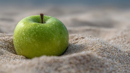 Negative space around a green apple on a sandy backdrop