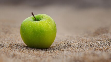Negative space around a green apple on a sandy backdrop