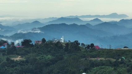 Sajek, Bangladesh - 21 August 2025: Aerial view of a white mosque and buildings atop lush green hills, contrasting with the distant blue mountain ranges.