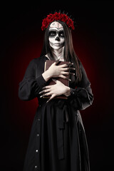 Young woman with calavera (sugar skull) makeup holds book (grimoire) in hands. The witch girl with...
