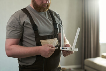 Middle aged Caucasian man holding wireless router and preparing to connect ethernet cable, standing...