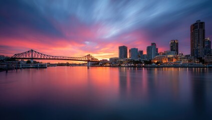 Fototapeta premium City skyline at sunset, reflected in a calm river. Dramatic colors of pink, orange, and purple in a twilight sky, streaked with clouds.
