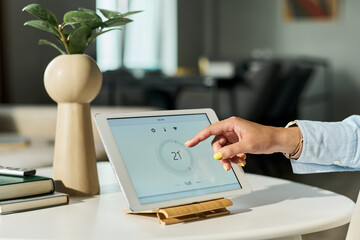 Caucasian young adult woman using tablet controlling smart home system, hand interacting with digital interface on screen, modern technology concept, indoor setting