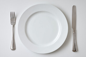 A round white plate is positioned center with a fork on the left and a knife on the right, set for a meal in a western dining atmosphere