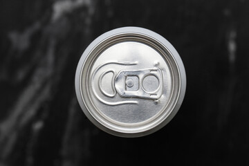 Top view of closed aluminum can with silver pull tab on black background. Macro shot of metal beverage container lid. Soda or beer packaging design element. Refreshing drink concept closeup.