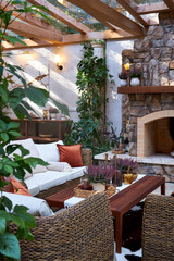 Cozy rustic living space with stone fireplace, wicker armchairs, and decorative plants. Warm autumn atmosphere in a stylish country house interior with natural textures and soft lighting
