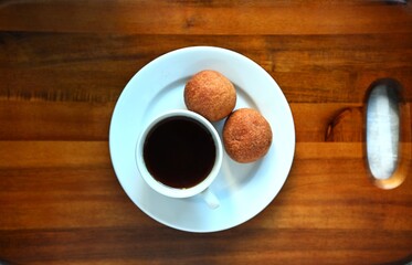 Cup of black coffee with two fresh buns served on a white plate on wooden table. Minimalist breakfast concept, top view.