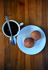 Cup of hot black coffee with two golden-brown donuts on a white plate, placed on a rustic wooden table. Cozy breakfast scene symbolizing comfort, simplicity, and morning relaxation.