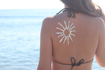 Sun image made with sunscreen on woman's back. Sunbathing on the beach. Close-up. Woman in swimsuit on the beach, back view. Using sunscreen. Concept of beach vacation, seaside resort, beach holiday