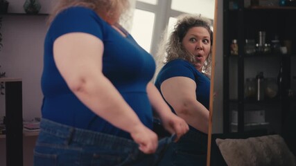 Happy large-bodied woman wearing oversized jeans, celebrating weight loss result