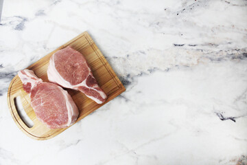 Two raw pork steaks lying on a wooden plank top view copyspace