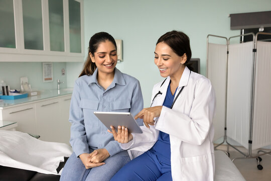 Happy diverse female doctor and patient watching video on tablet