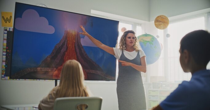 Geology Class: Female Teacher Teaching Primary School Children Using Digital Screen. Group of Young Students Sitting at the Desks, Learning Eruption of the Volcano and Geography in Modern Classroom. - Powered by Adobe