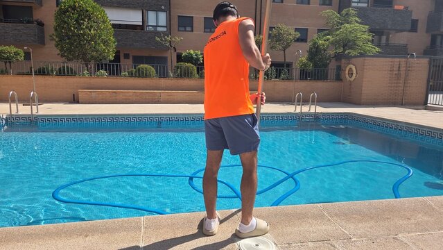 Summer pool maintenance with person cleaning residential swimming area. Lifeguard cleaning the pool in the urbanization