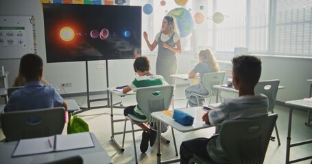 Elementary School Students Studying Basic Information About Solar System and Planets in Modern Classroom. Female Teacher Educating Smart Diverse Kids During Astronomy Lesson Using Digital Screen.