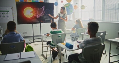 Elementary School Students Studying Basic Information About Solar System and Planets in Modern Classroom. Female Teacher Educating Smart Diverse Kids During Astronomy Lesson Using Digital Screen.