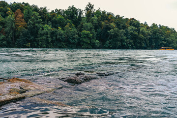 Majestic view of Rhine Falls, the largest waterfall in Europe, located near Schaffhausen in northern Switzerland. Powerful cascades of water rush over rugged rocks, surrounded by lush greenery and mis