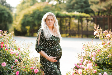 Stylish pregnant woman 30-35 year old wearing dress in floral meadow with flowers outdoors....