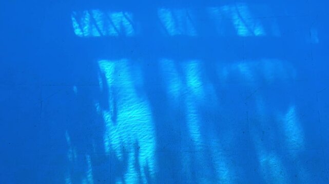 Moving shadow reflections on the bottom of a blue swimming pool illuminated by sunlight