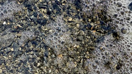 shimmering river pebbles under clear water with natural bubble clusters creating abstract stone surface texture for background or design