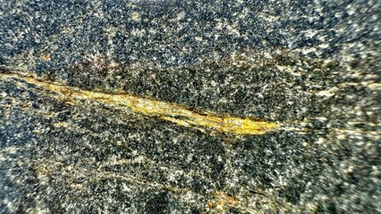 close up of dark granite stone surface with golden mineral vein detail for natural background or texture design
