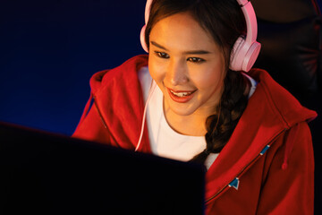Portrait host channel of beautiful Asian girl streamer playing online game wearing headphones pastel color talking with viewers media online. Esport skilled team players in neon blue room. Stratagem.