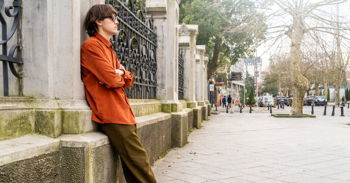Stylish young man in vintage outfit leaning on historic stone wall in quiet city street. Urban lifestyle, retro fashion, alternative youth culture. - Powered by Adobe