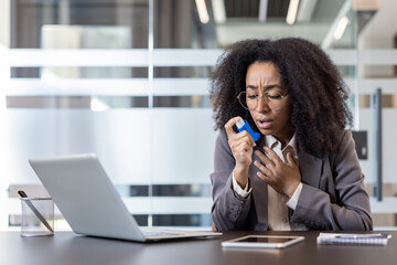 Young African American businesswoman suffering from asthma, sitting at a desk in the office and...