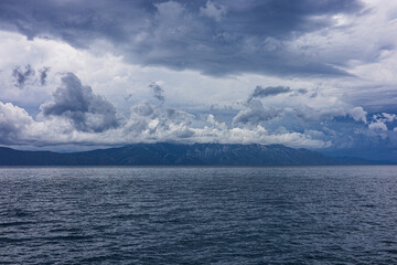 Stormy sky over mountains and sea. Dark dramatic clouds hang over the water surface, creating an...